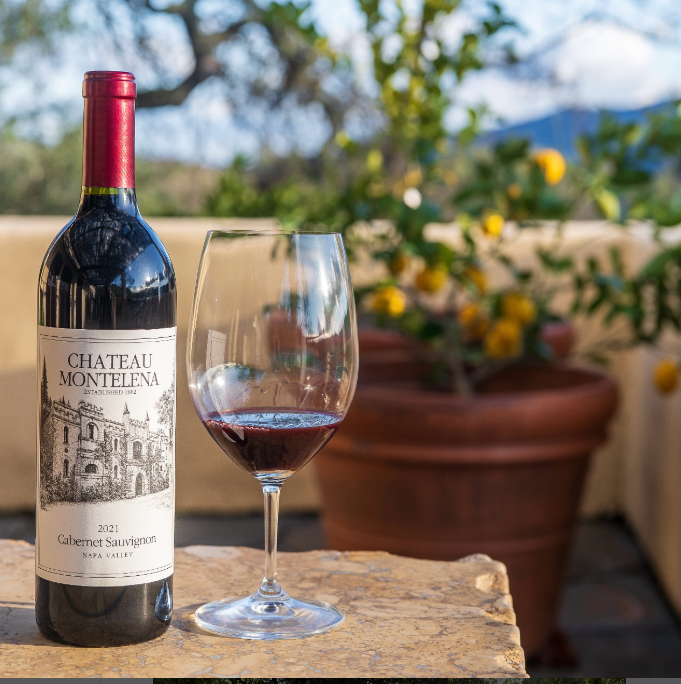 Chateau Montelena wine bottle with a glass of red wine on a wooden surface outdoors.