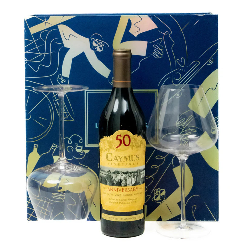 Caymus Anniversary wine bottle with two glasses against a decorative blue background