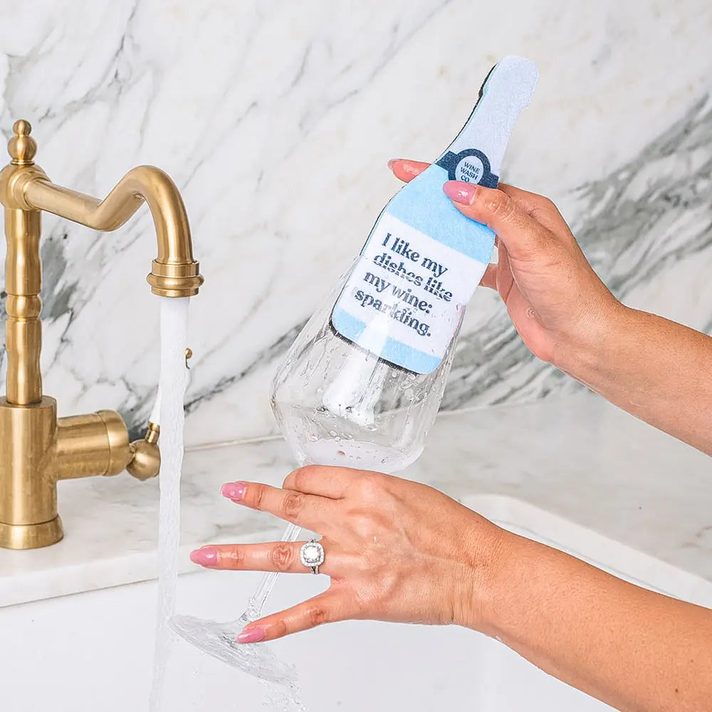 Person washing a bottle with a humorous label under a running faucet.