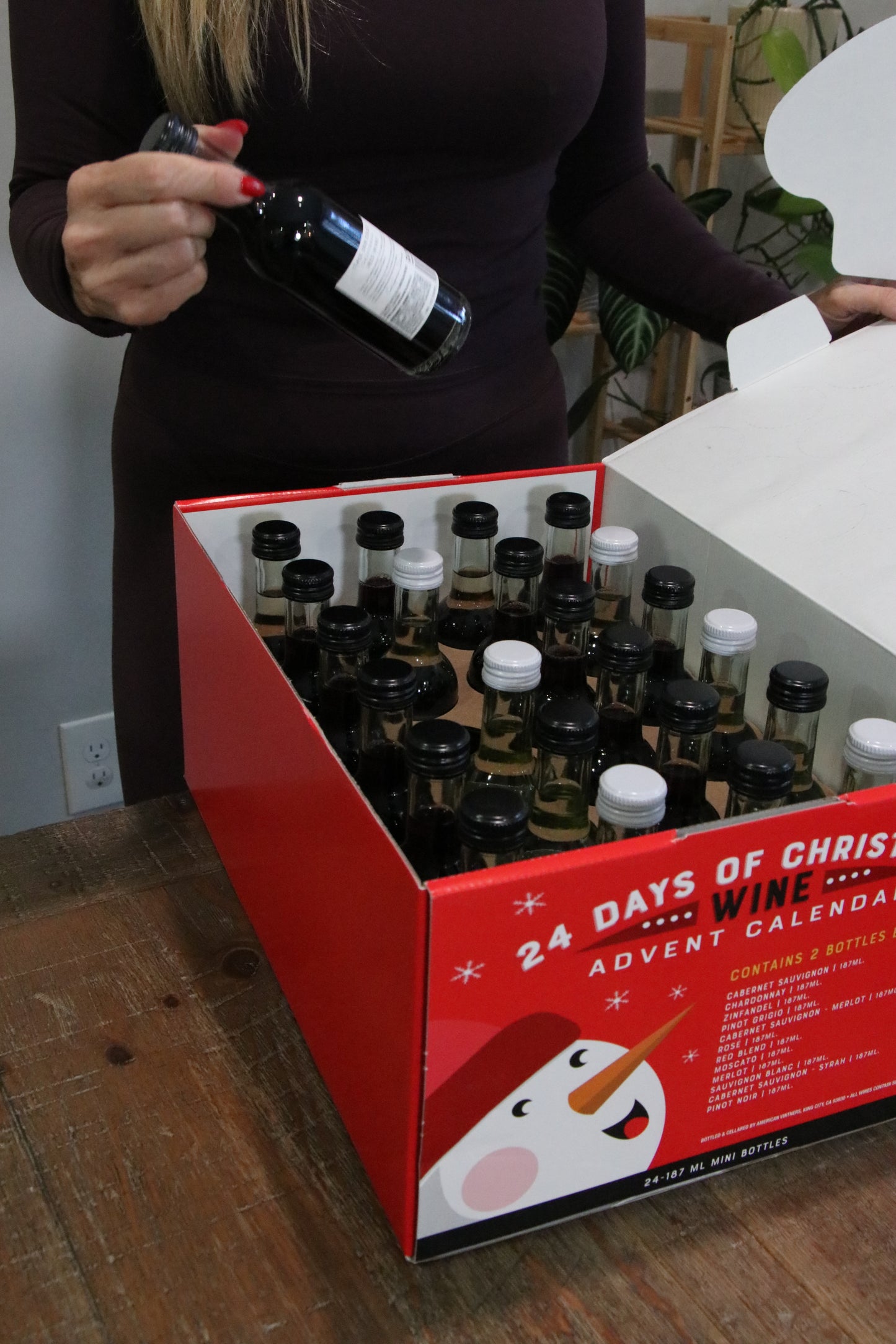 Person holding a bottle of wine next to a 24-day Christmas advent calendar on a wooden surface.