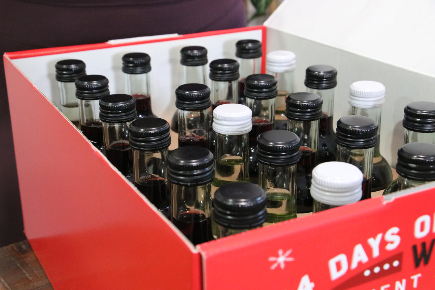 Collection of small glass bottles with black and white caps in a red box.